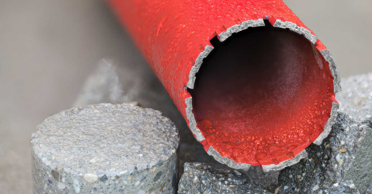 red water cooled diamond core drill bit on round bored piece of gray concrete tile closeup